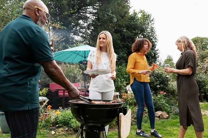 A group of people gathered in a backyard, enjoying a BBQ party with delicious food on the grill, colorful decorations, and happy conversations.