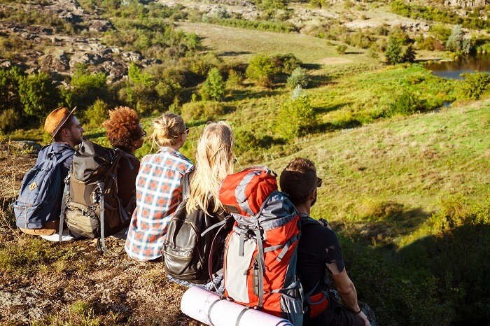 A group of young adults hiking in the mountains with backpacks, taking in the scenic views of nature and enjoying the adventure.