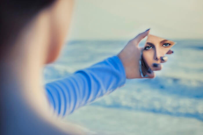 A person looking into a mirror surrounded by thought bubbles, symbolizing self-awareness and reflection.